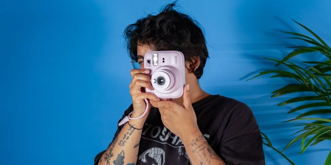 Mavi fonda pembe Fujifilm Instax Mini 13 ile fotoğraf çeken kişi