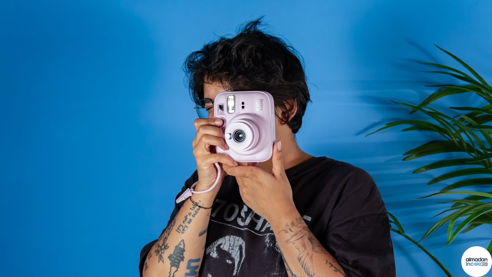 Mavi fonda pembe Fujifilm Instax Mini 13 ile fotoğraf çeken kişi
